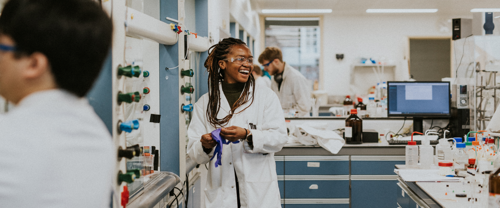 Research in the University of Bristol School of Chemistry lab smiles as she puts on protective gloves
